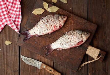 fresh crucian fish sprinkled with spices lies on a brown wooden cutting board, wooden table from boards, top viewの写真素材