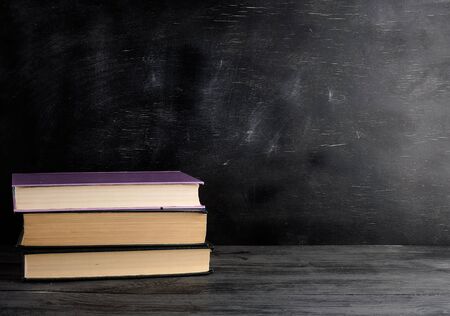 four closed books with yellow sheets on a black chalk board background, copy space, back to school conceptの写真素材
