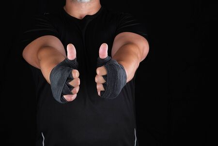 sportsman's hands wrapped in black elastic sports bandage show a like sign, dark backgroundの写真素材