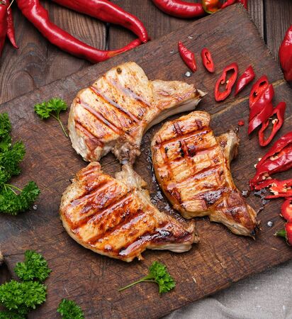 pork fried steak on the rib lies on a vintage brown wooden board, next to fresh red chili peppers, top viewの写真素材
