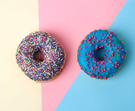 round baked donut with colored sugar sprinkles and with blue sugar glaze on a pink-yellow...