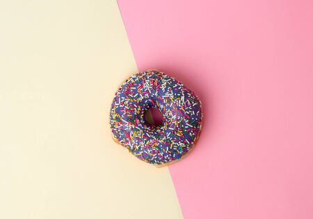 round baked donut with colored sugar sprinkles on a pink-yellow background, top viewの写真素材