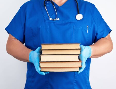 doctor in blue uniform and sterile latex gloves holds a stack of books in his hand against a white background, man stands in frontの写真素材