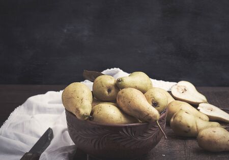fresh ripe green pears in a brown clay bowl on a table, close upの写真素材
