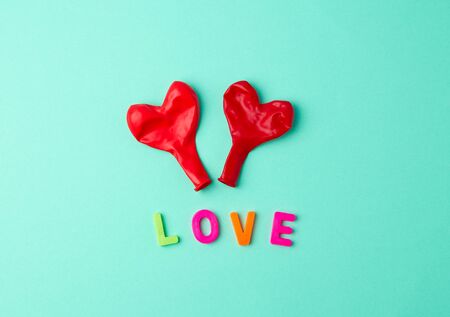 two red rubber balloons blow away in the shape of a heart on a green backgroundの写真素材