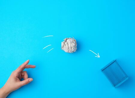 hand pushed a ball of crumpled gray paper into a metal wastebasket, concept of waste recycling and environmental pollution