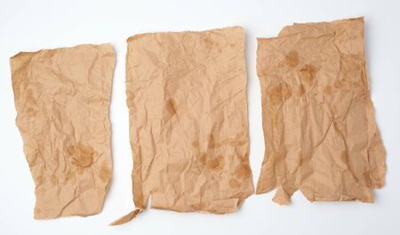 three torn crumpled pieces of brown paper with grease stains on a white background, top viewの写真素材