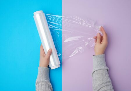 two hands hold a large roll of wound white transparent film for wrapping food, top viewの写真素材