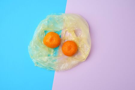 two ripe orange mandarins lie in a transparent plastic bag on a color background, top viewの写真素材