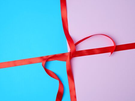 red satin ribbon on a colored background, imitation of tying and packing a giftの写真素材