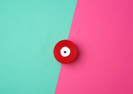 spools with red satin ribbon on a green pink background, top view