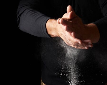 man claps his hands and scatters to the side a white substance on a black background, magnesia for rubbing hands, selective focusの写真素材