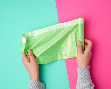 female hand unwinds a green plastic bag for rubbish, green pink background