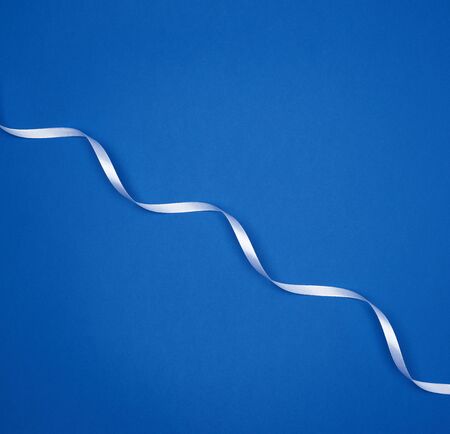 white silk thin ribbon twisted on a blue background, trendy classic color, top viewの写真素材