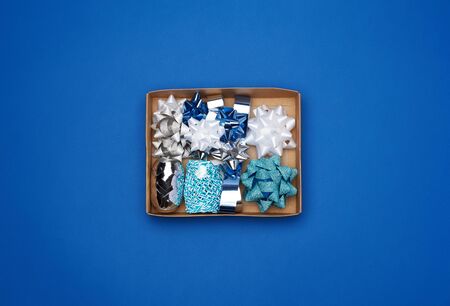 brown cardboard box with a set of decor ribbons and bows for wrapping gifts on a dark blue...