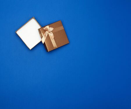 open brown square cardboard empty box, item lies on a blue classic background color, top view, copy...