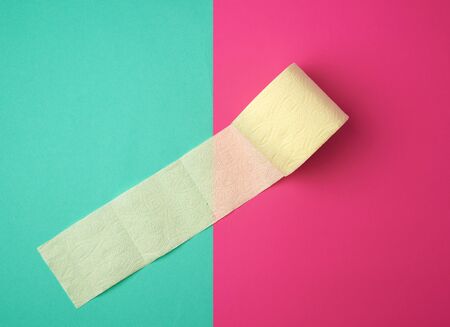 soft yellow toilet paper in a roll on a green-pink background, top view