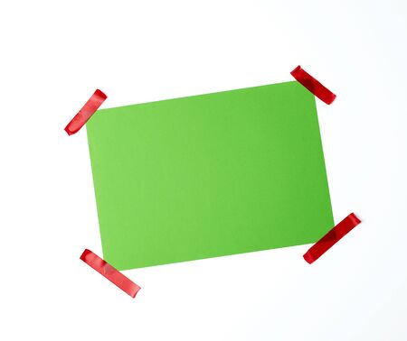 blank green sheet of paper stuck with red sticky tape on a white background, place for textの写真素材