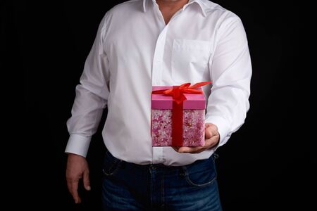 adult man in a white shirt holds a pink gift cardboard box with a bow, concept of a congratulation on the holiday, anniversary, surpriseの写真素材