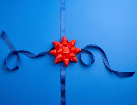 blue silk ribbon crossed on a dark blue background in the middle of a red bow, imitation of tying a gift, top viewの写真素材