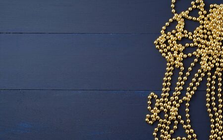 Christmas garland of round golden beads strung on a string, blue wooden background from boards. Golden garland ball christmas shine in beautiful style, copy spaceの写真素材