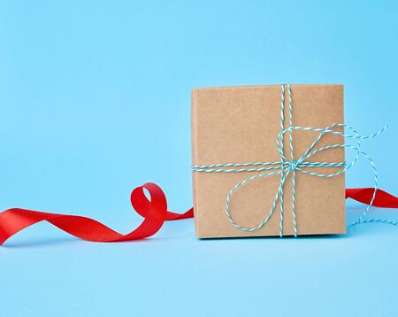 square brown cardboard box for a gift and twisted silk red ribbon on a blue background. Beautiful box gift, great design for any purposes. の写真素材