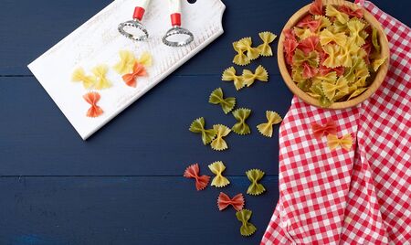 raw pasta in the form of bows in a wooden round plate and white textile napkin on a blue wooden...