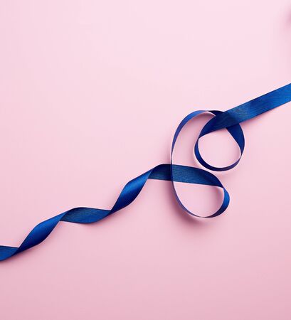 blue silk thin ribbon twisted on a pink background, close upの写真素材