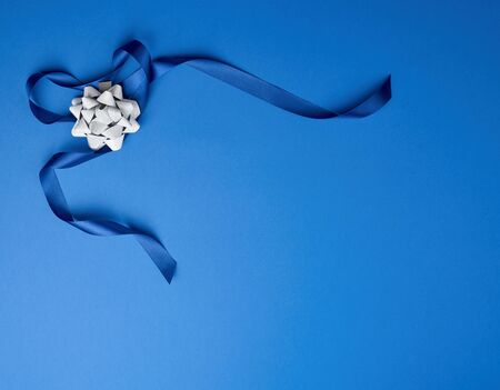 blue silk thin ribbon twisted and gray shiny bow on a blue background, trendy classic color, copy...