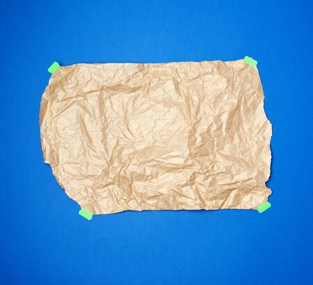 crumpled brown sheet of parchment paper glued with green paper   on a blue background. Copy space