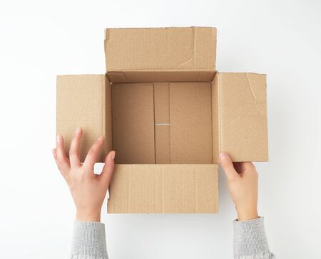 open empty square brown cardboard box for transportation and packaging of goods and two hands take...