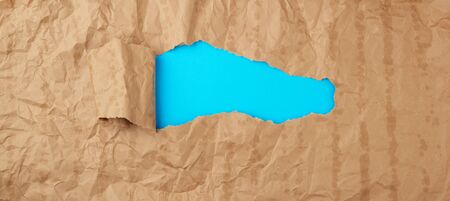 crumpled paper texture from a brown sheet of paper with greasy spots and a large hole with a twisted corner, abstract banner for the designer, blue backdrop. Vintage template with brown paper hole curlingの写真素材