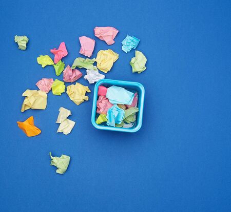 stationery blue metal bucket filled with crumpled multi-colored stickers, top view, blue backgroundの写真素材