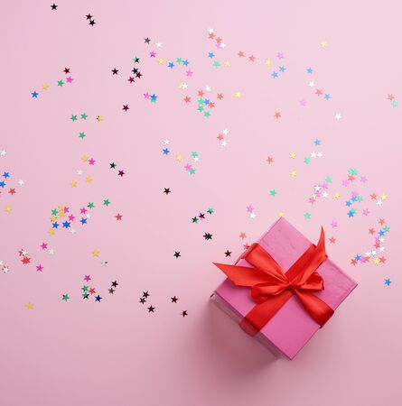 beautiful pink closed box with a big bow on a pink background with multi-colored sparkles, concept of congratulations and surprise, top viewの写真素材