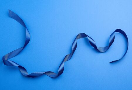 blue silk thin ribbon twisted on a blue background, trendy classic color, close upの写真素材