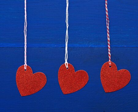paper red shiny decorative hearts hanging on a rope on a dark blue wooden background, abstract holiday backdrop for valentines day on february 14の写真素材