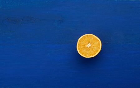 half ripe juicy orange on a dark blue wooden background, abstract trendy backdrop with fruit in a minimalist styleの写真素材