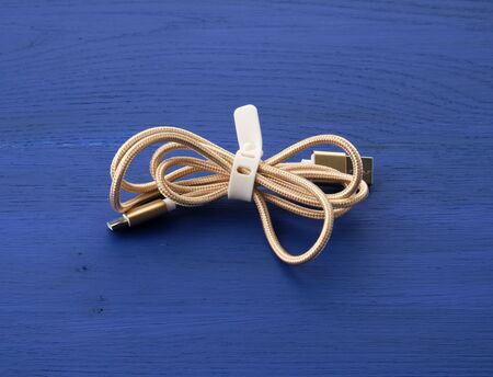 twisted golden cable for charging with electricity equipment in textile winding on a blue wooden background, close upの写真素材