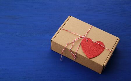 rectangular brown box with a gift and a red paper heart tied to a rope, blue wooden background, top view, copy spaceの写真素材