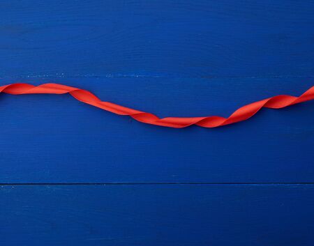 red silk thin ribbon twisted on a blue wooden background, trendy classic color, top viewの写真素材
