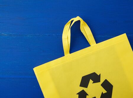 Reusable yellow viscose bag on blue wooden background, plastic waste reduction concept