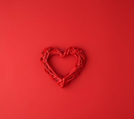 red wicker decorative heart on a red paper background, festive backdrop for Valentine's day
