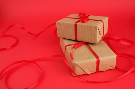 box wrapped in brown kraft paper and tied with a red thin silk ribbon on a red background, holiday...