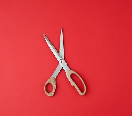iron scissors with a beige plastic handle on a red background, top view, flat lay