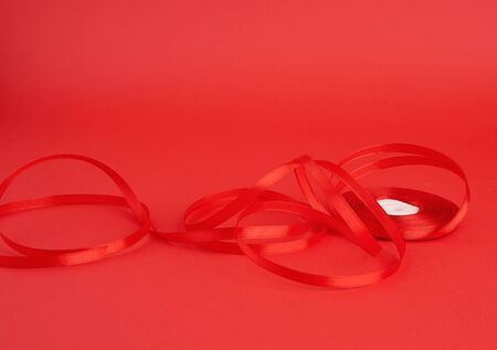 twisted red silk shiny ribbon on a red background, festive design element, close up