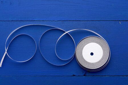 one round bobbin with silver ribbon on a blue wooden background, top viewの写真素材