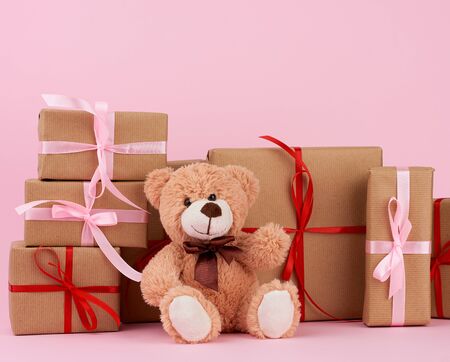 brown cute teddy bear and gifts wrapped in brown eco kraft paper and tied with a ribbon on a pink...