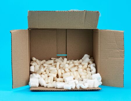 open rectangular brown cardboard box with white foam filling for transporting goods on a blue backgroundの写真素材