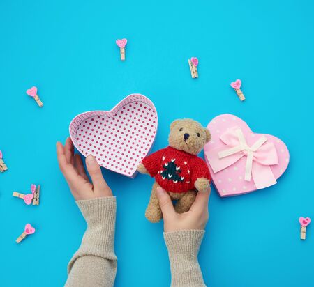 female hands holding a small brown teddy bear, on a blue background an open empty heart-shaped box, top view, holiday Valentine's Dayの写真素材