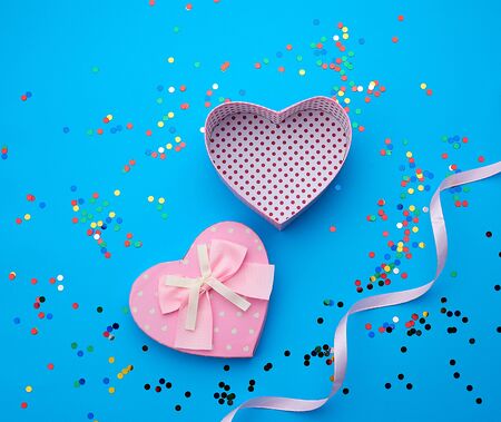open pink heart-shaped cardboard box on a pink background with multi-colored shiny confetti, festive backdrop for birthday, Valentine's dayの写真素材